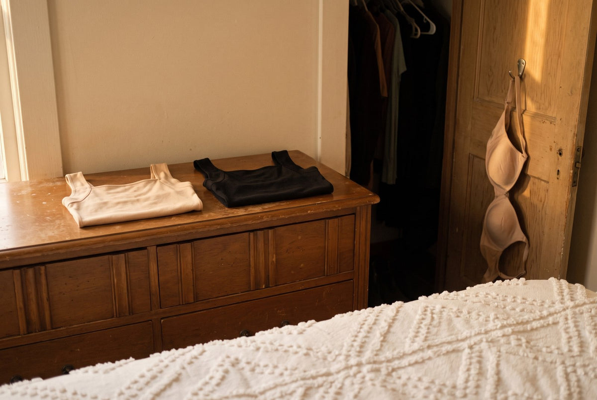 The same white bedspread in late-day golden light. The empty drawer slid back into the old dresser, a nude tank and a bl